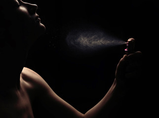 Young woman with spraying perfume on black background