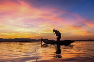 Naklejka na ściany i meble Silhouette fisherman on fishing boat setting net with sunrise