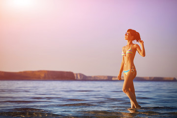 beautiful sexy woman dressed in bikini walking on the beach along the sea front