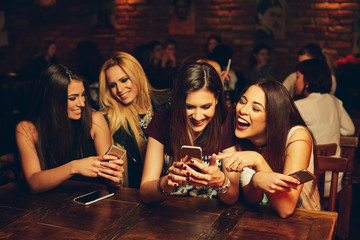 group of young women friends having fun looking at something funny on their smart phone and laughing