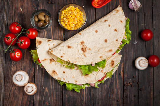 Sandwiches twisted roll Tortilla two pieces and vegetables on a wooden background