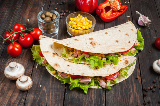 Sandwiches twisted roll Tortilla two pieces and vegetables on a wooden background