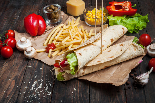 Sandwiches twisted roll Tortilla two pieces and french fries on a wooden background