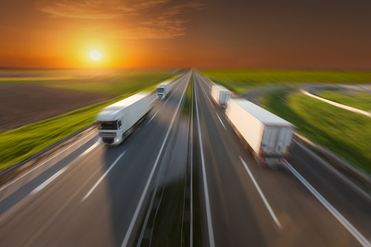 Reefer trucks in motion blur on the empty freeway at sunset