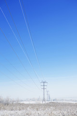 Winter industrial landscape high-voltage lines in the snow-covered field near the forest