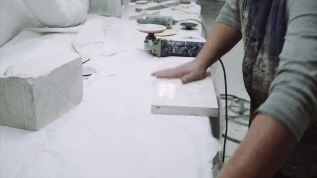 Worker polishes the piece of marble stone with tools