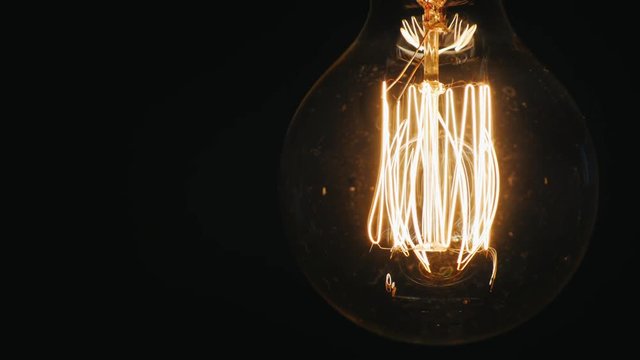 Old light bulb lights up continuously. On a black background, slightly swaying