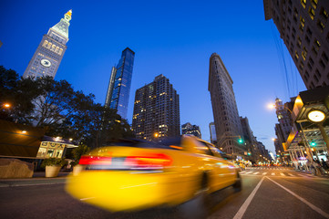 Defocus motion blur view of yellow taxis driving through the city streets at dusk in New York City,...