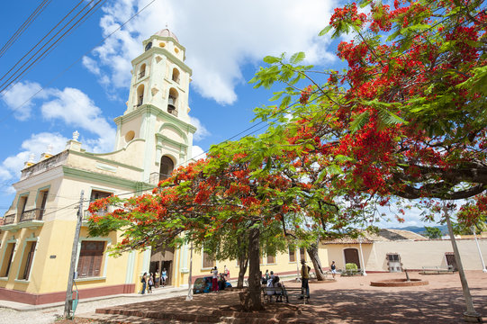 Traditional colonial church architecture of San Francisco de Asis in Trinidad, Cuba with tropical flame tree in full bloom in the town plaza
