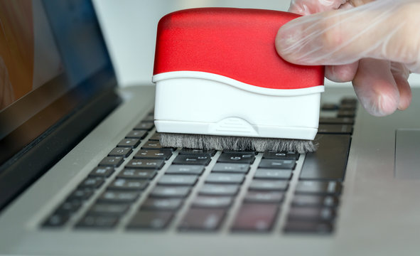 Person cleaning computer keyboard with brush tool