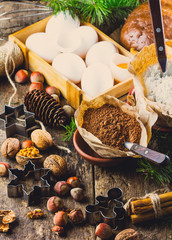 Christmas or New Year baking cake background. Dough, dough ingredients - flour, chocolate, walnuts, hazelnuts, sugar eggs cinnamon and Christmas decorations on wooden rustic background