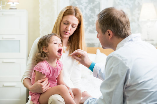 Male Pediatrician examining throat of a little ill girl. Kid looks sick and sad. Mother holding her kid. Doctor visit his patient with high fever at home. Doctor examining child with thermometer.
