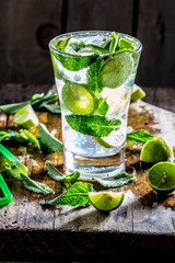 Glass of alcohol cocktail or lemonade. Mohito cocktail with lemon, lime, mint, ise cubes. Cold drink. Fresh lime and mint on wooden background