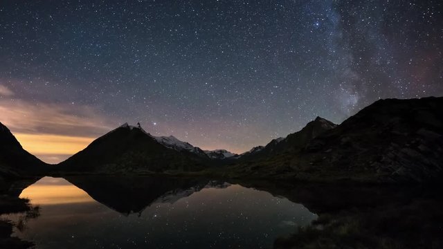 The apparent rotation of the Milky Way and the starry sky beyond snowcapped mountain ridge, reflected on idyllic apine lake. Orion Constellation coming from left at the end. Time Lapse 4k video.