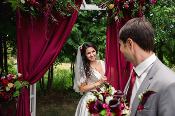 Wedding. Elegant groom looking at beautiful bride who is standing near the wedding arch. Colorful wedding