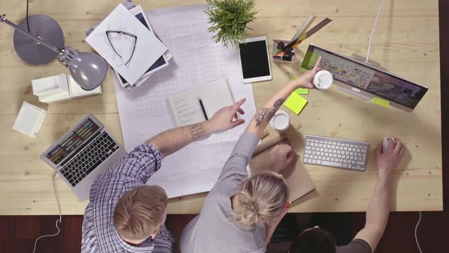 Top view of three designers working in team on house project. They choosing and discussing colors at the computer screen
