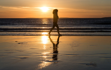 silhouette of woman walking on the beach at sunset