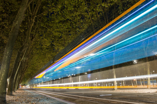 Tram speeding through wooded park area in downtown Bordeaux at night