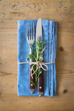 Fork, knife and napkin decorated with rosemary and thyme on rustic wooden background