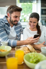 Couple using mobile phone while having breakfast