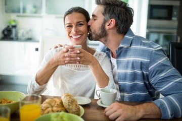 Man kissing on woman cheeks while having breakfast