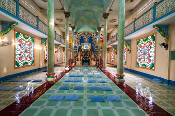 Fototapeta na wymiar View to interior of Buddhist temple with high columns and bright colorful walls. Pillows for pray are laying down on the floor before an Buddhist deity altar