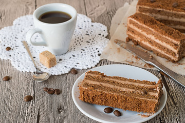 
 Pieces of chocolate cake on parchment paper and on a white plate, a cup of coffee on a napkin, on a gray wooden table.