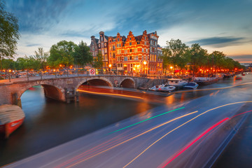 Amsterdam canal, bridge and typical houses, boats and luminous track from the boat during morning...