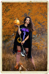 Young woman in Halloween witch costume in the autumn forest with yellow pumpkin.