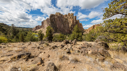 Large stones in the dry grass. The river flows between rocks. Beautiful landscape of yellow sharp cliffs. Dry yellow grass grows at the foot of cliffs. Smith Rock state park, Oregon