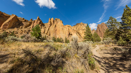 The path among the rocks. The sheer rock walls. Beautiful landscape of yellow sharp cliffs. Dry yellow grass grows on the slopes of the mountains. Smith Rock state park, Oregon