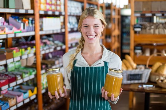 Smiling female staff holding jars of honey in supermarket