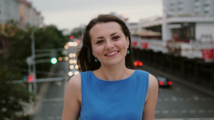 Wind blows long dark hair beautiful young women. happy, smiling girl standing on the bridge and looks at the camera. 4K