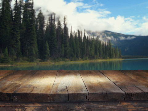 Fototapeta Empty wooden table in front of fir forest and snowy mountains