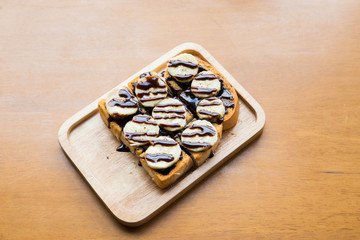 Banana with chocolate on grilled bread on wooden dish