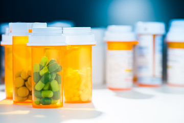 Numerous pill bottles of different prescription capsule tablet pill medicine medications in dramatic blue atmosphere