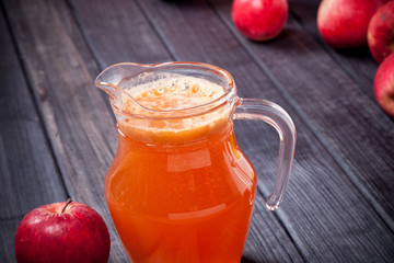 red apples and fresh juice with foam in the pitcher on table