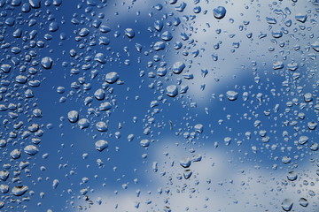 Rain drops on window with blue cloudy sky in background , spring rainy day