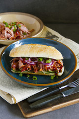 Sandwich with pulled pork, onion and cucumber. Newspaper, wooden board, gray background. 