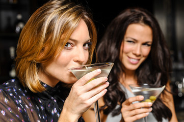 Two attractive young women drinking martinis in nightclub bar atmosphere