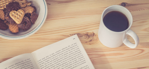 Schreibtisch / Arbeitsplatz mit Buch, Kafeetasse und Keksen, Breitbild retro 