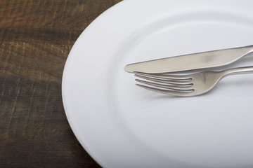 Empty white dish with spoon and fork on wood table