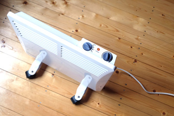 Working white electric convector heater with control panel on top on wooden floor in a house room top view closeup