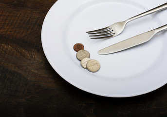 Plate with coins and knife with fork on wooden background
