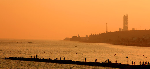 People fishing on a pier with the sea in the background in the orange light of the late afternoon in Spain.