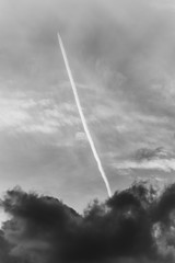 Airplane with Contrail in cloudy sky in black and white