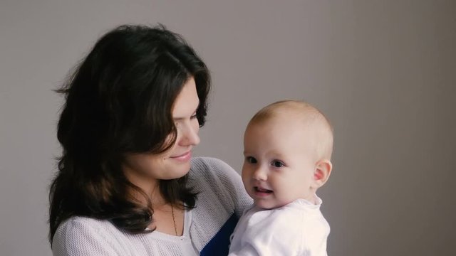 Young Happy Mother Holding her Newborn Child. Family at home. Beautiful smiling Mom and Happy Baby Together.