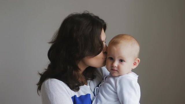 Young Happy Mother Holding her Newborn Child. Family at home. Beautiful smiling Mom and Happy Baby Together.