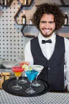 Bartender holding tray of cocktails and milkshake in bar 