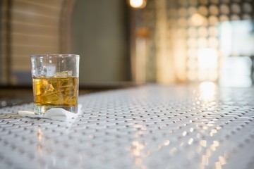 Glass of whisky with ice cube on bar counter